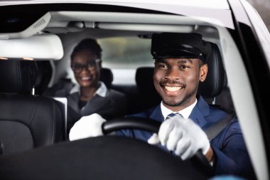 Businesswoman Sitting Behind Happy African Male Chauffeur Driving Car clipart