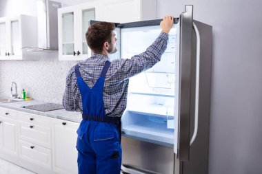 Serviceman Checking Temperature Of Refrigerator In Kitchen clipart