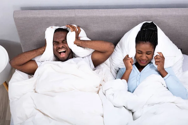 非洲的年轻夫妇在床上用枕头捂住耳朵而感到不安 — 图库照片