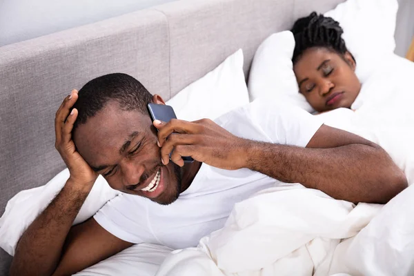 Gülümseyen genç Afrika adam akıllı yatak yatak odasında uyuyan karısını yanında konuşmak