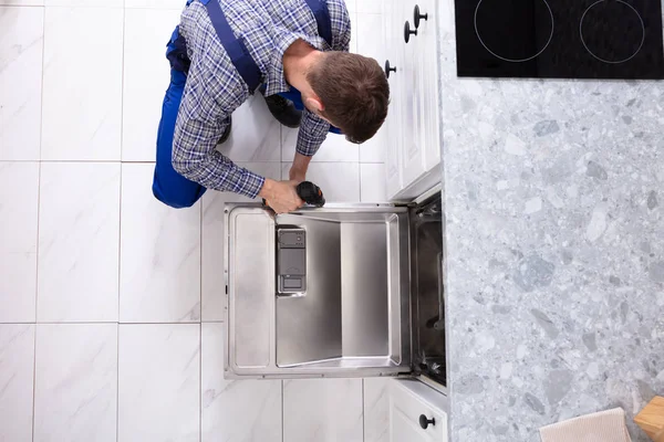 Genç tamirci mutfakta bulaşık makinesi elektrikli matkap ile sabitleme