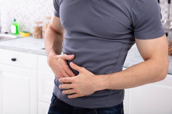 Молодой человек страдает от желудка Ache стоя на кухне дома
