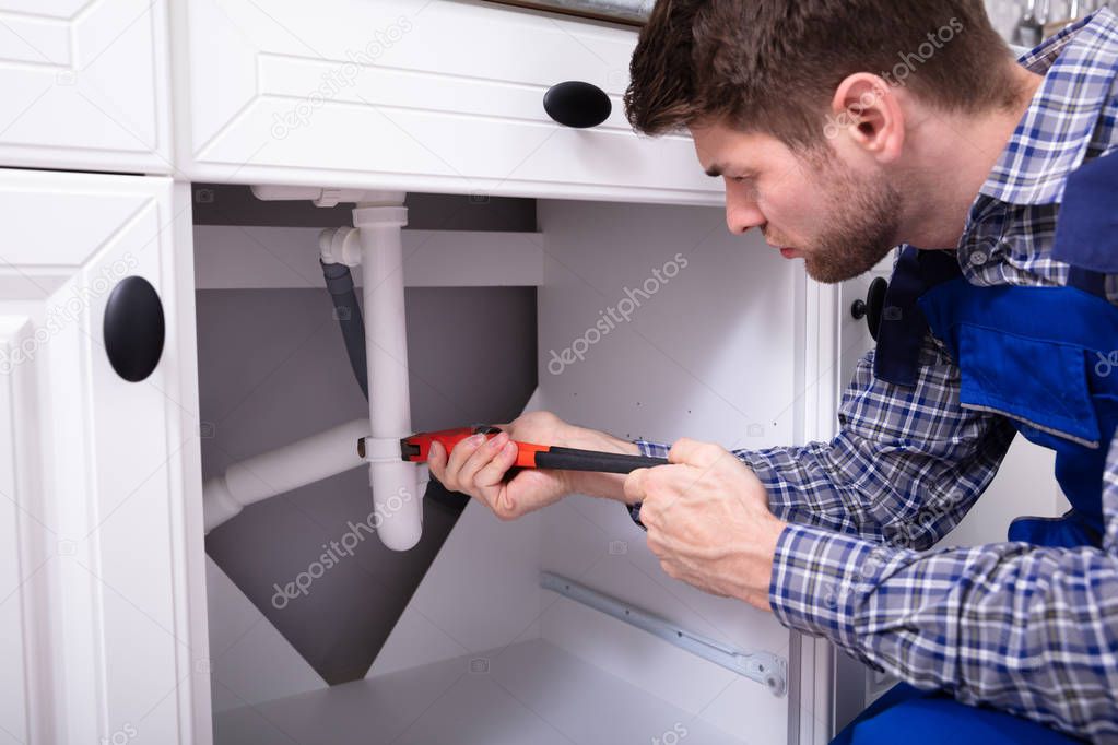 Young Male Plumber Repairing Sink Pipe With Adjustable Wrench