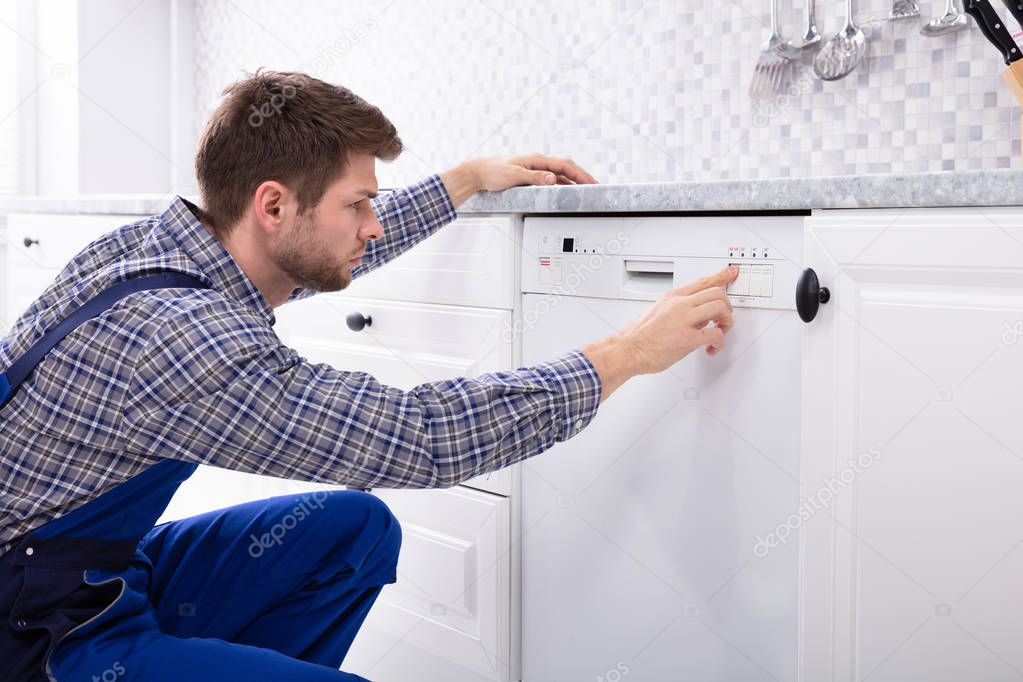 Young Serviceman Pressing Button Of Dishwasher In Kitchen