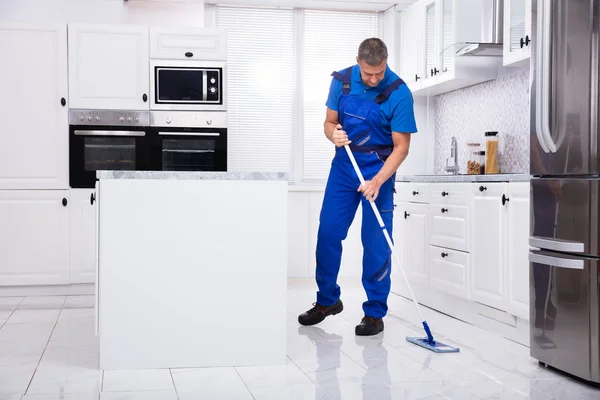 侧视图的男性看门人清洁白色地板与拖把在厨房 — 图库照片