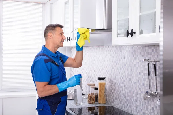 キッチンでナプキンとスプレー洗剤と成熟した男性ジャンタークリーニングクッカーフード — ストック写真