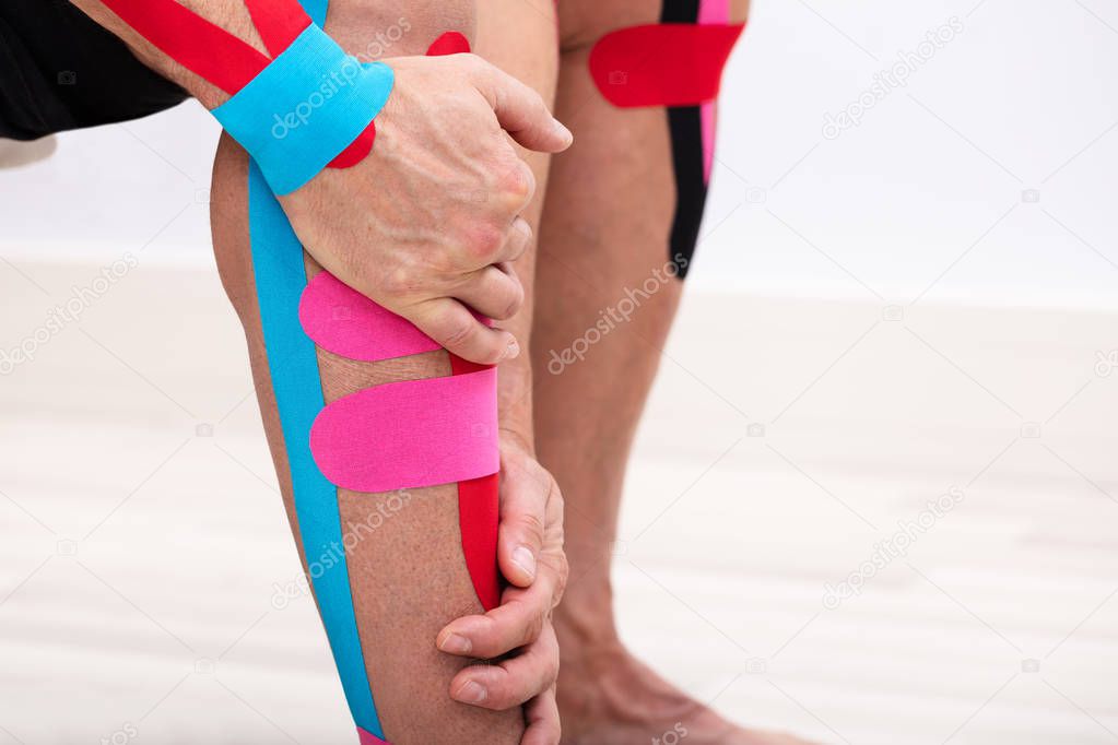 Close-up Of Man Applying Kinesiology Tape On His Leg