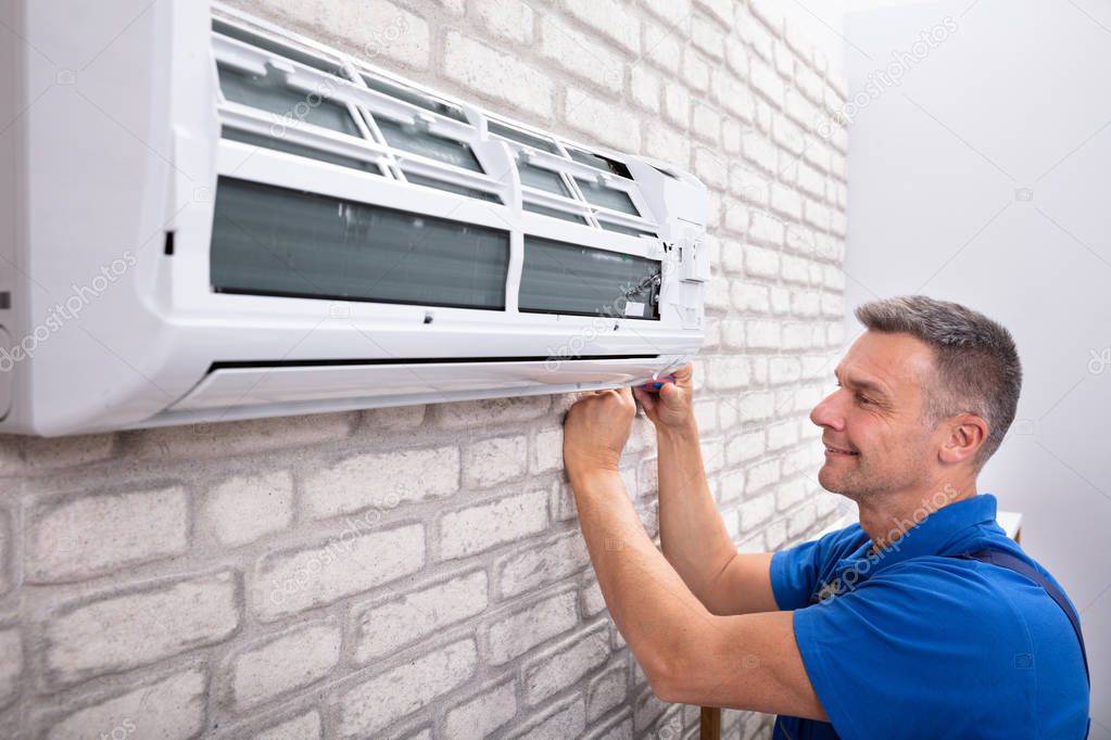 Mature Male Technician Fixing Air Conditioner With Screwdriver