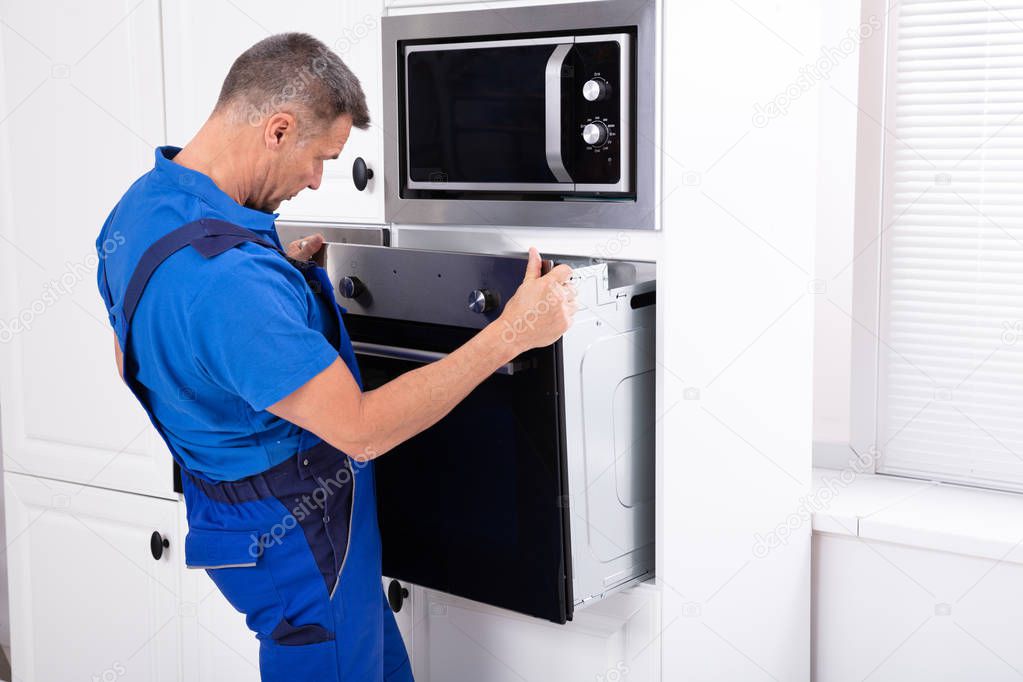 Male Technician Wearing Overall Installing Oven In Kitchen