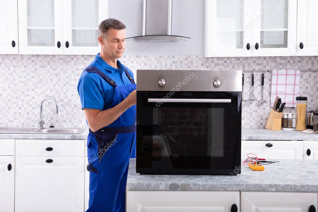 Mature Male Technician Repairing Oven On Kitchen Worktop