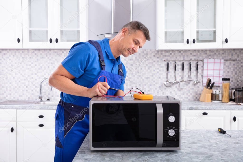 Male Handyman Repairing Microwave Using Digital Multimeter In Kitchen