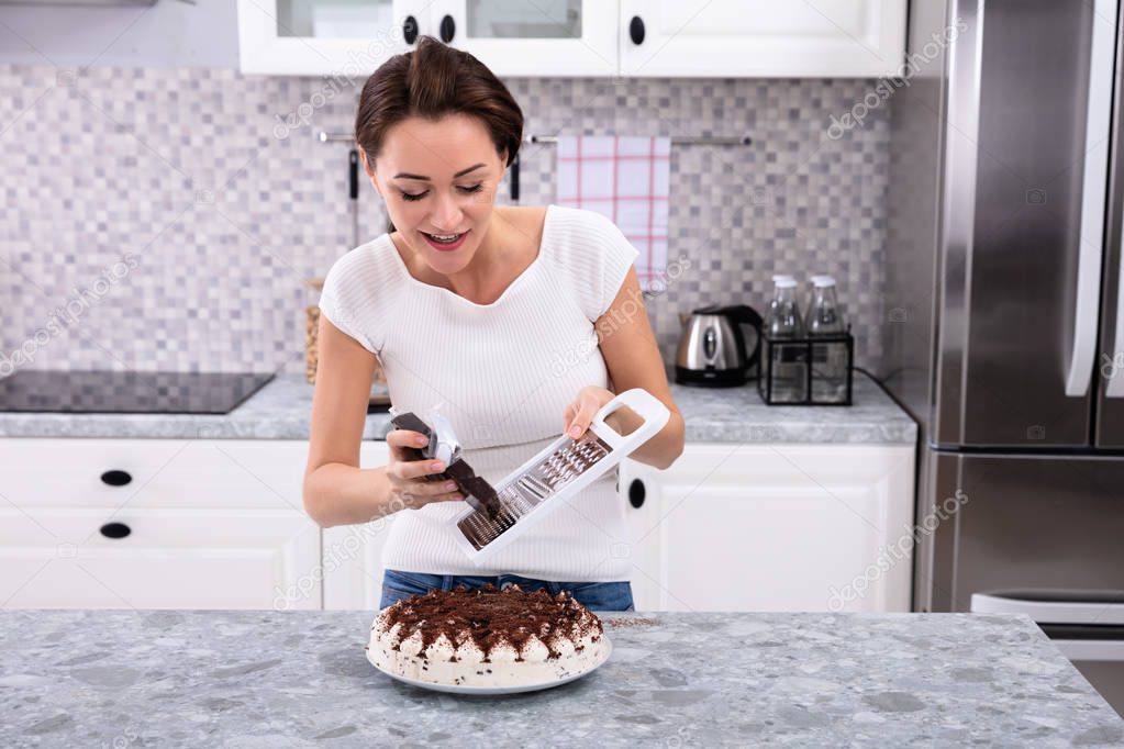 Portrait Of A Smiling Young Woman Grating Chocolate Over Cake