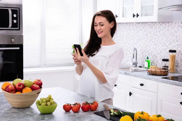 Sorrindo Jovem Mulher Usando Celular Perto Frutas Frescas Legumes Balcão — Fotografia de Stock