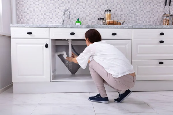 一个女人试图阻止厨房水槽管道漏水的后视图 — 图库照片