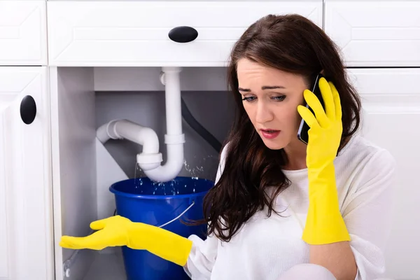 Sad Young Woman Calling Plumber Front Water Leaking Sink Pipe — Stock Photo, Image