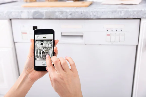 携帯電話で食器洗い機を操作する女性の手のクローズアップ — ストック写真