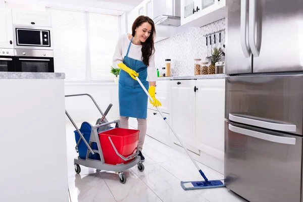 愉快的女性门卫清洁地板与拖把在厨房 — 图库照片