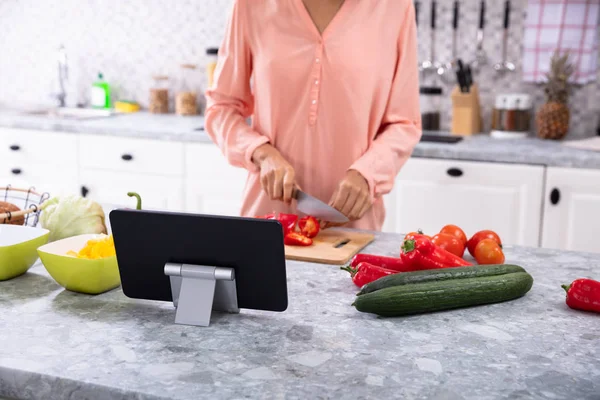 キッチンのまな板に赤ピーマンを切り込みながらデジタルタブレットを使う女 — ストック写真