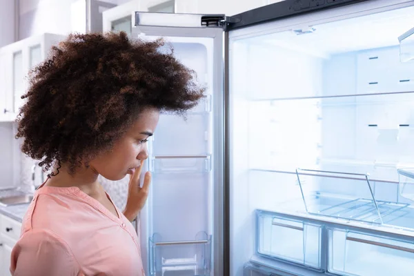 空の冷蔵庫を見てショックを受けたアフリカの若い女性のクローズ アップ — ストック写真