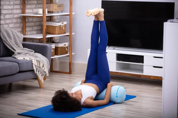 一个年轻女子在客厅里的瑜伽垫上做腿部运动 — 图库照片
