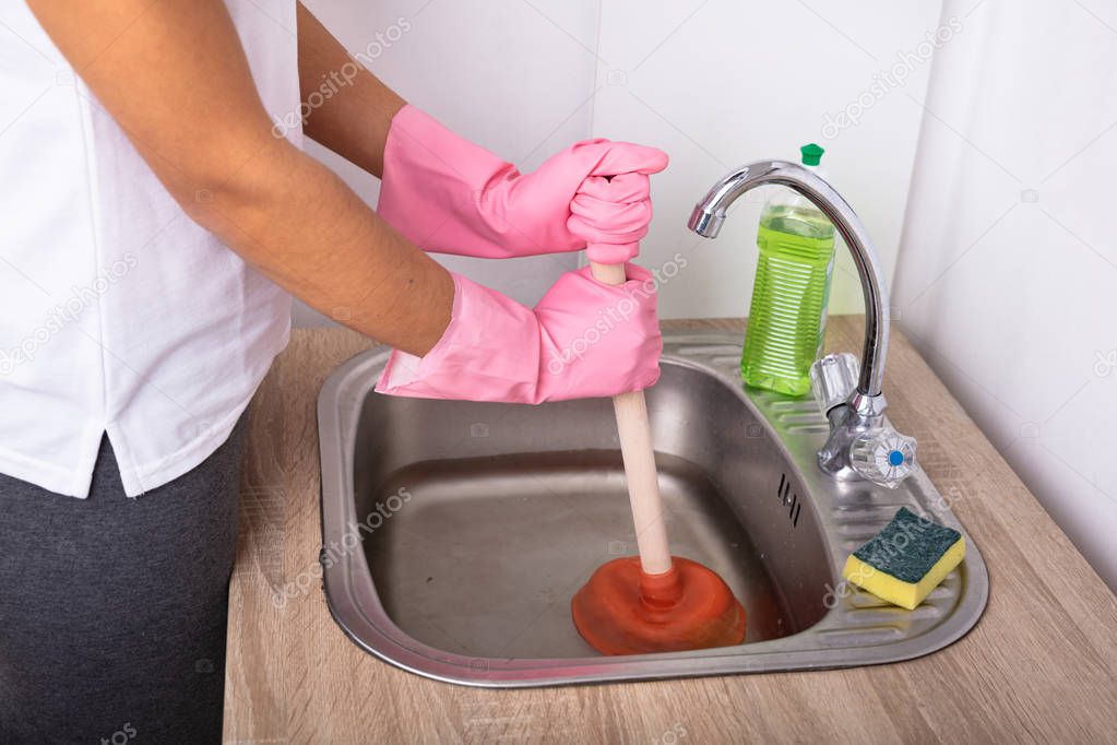 Close-up Of A Female Plumber Wearing Pink Gloves Using Plunger In The Kitchen Sink