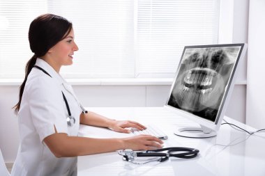 Kadın doktor klinikteki bilgisayardan diş röntgenine bakıyor.