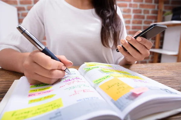 Närbild Affärskvinna Som Håller Mobiltelefon Skriva Schema Dagbok Med Penna — Stockfoto