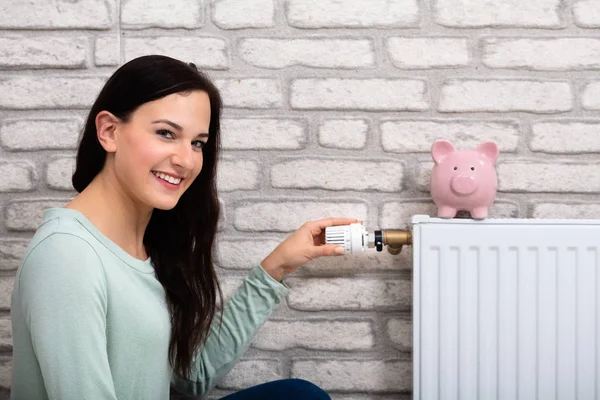 Jonge Lachende Vrouw Thermostaat Met Spaarvarken Radiator Thuis Aanpassen — Stockfoto