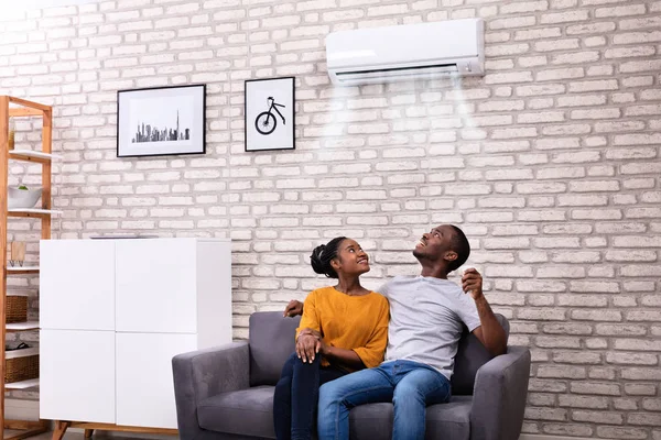 Young African Couple Sitting Sofa Operating Air Conditioner Home — Stock Photo, Image