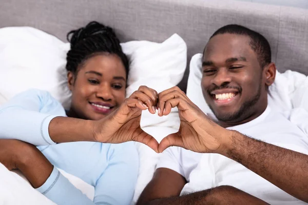 ハートの形を作ってベッドに横たわって幸せなアフリカのカップル — ストック写真