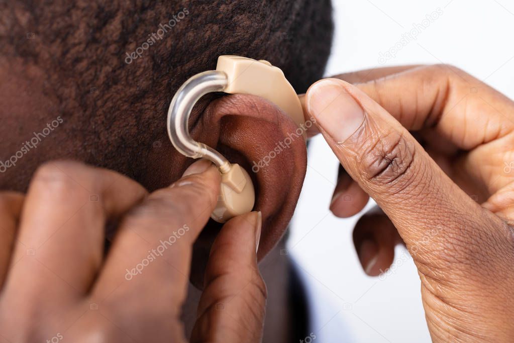 Close-up Of A Doctor's Hand Inserting Hearing Aid In Male Patient's Ear