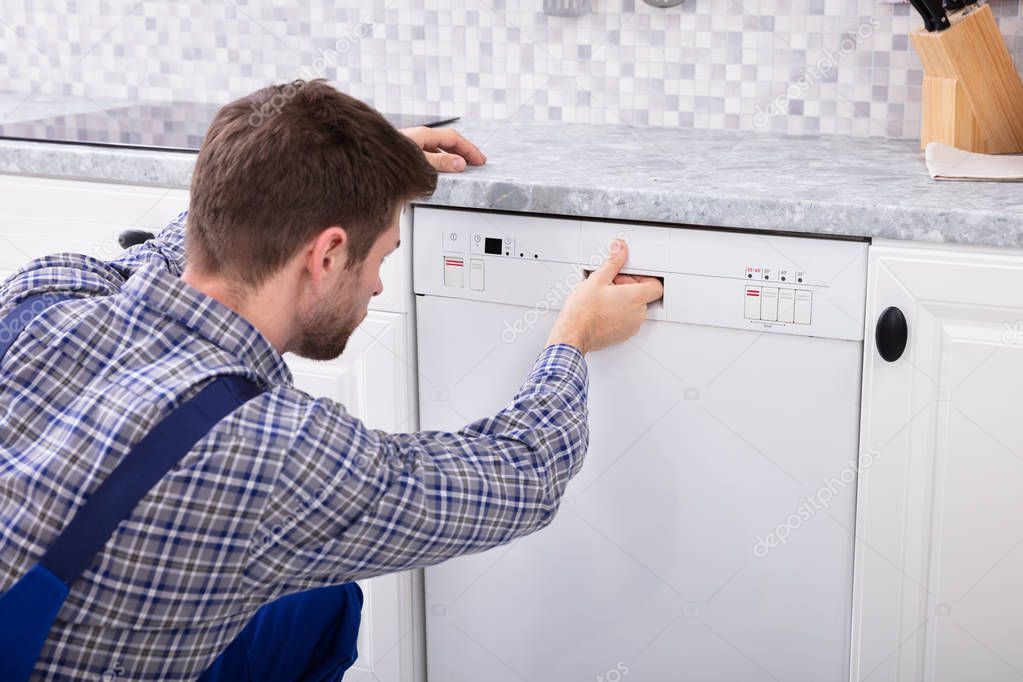 Young Serviceman Pressing Button Of Dishwasher In Kitchen