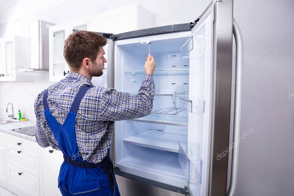Serviceman Checking Temperature Of Refrigerator In Kitchen