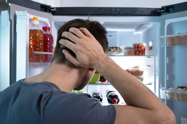 オープン冷蔵庫で食べ物を探す混乱した男 — ストック写真