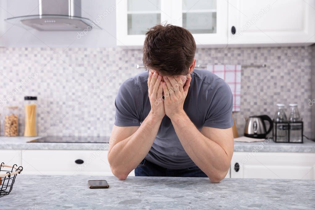 Frustrated Man Covering His Face With Two Hand Sitting In Kitchen