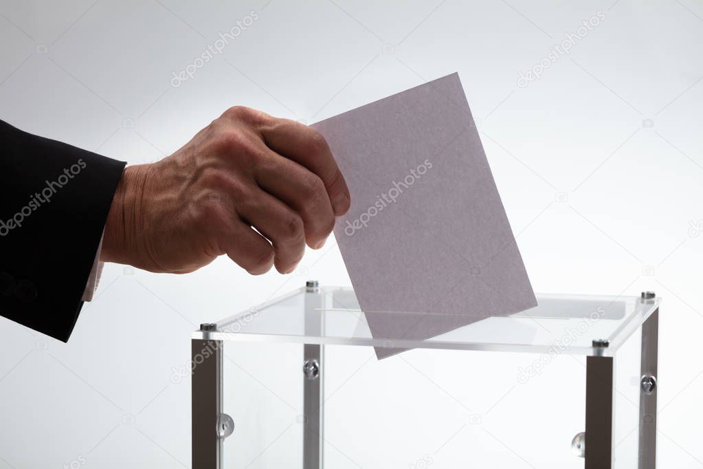 Close-up Of Businessman's Hand Inserting Ballot In A Glass Box