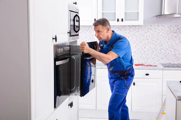 台所でオーブンを全体的にインストールを身に着けている男性技術者 — ストック写真