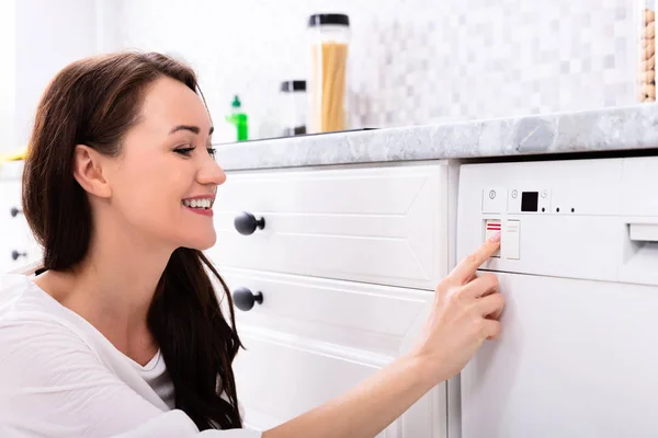 食器洗い機のボタンを押すと幸せな若い女の側面図 — ストック写真