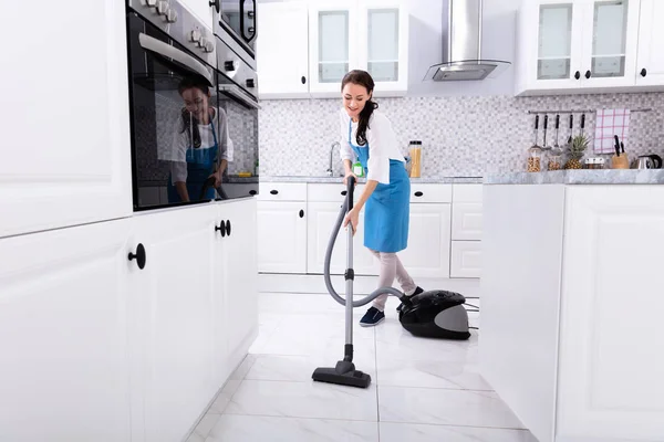 年轻的女看门人在统一清洁厨房地板真空地板 — 图库照片