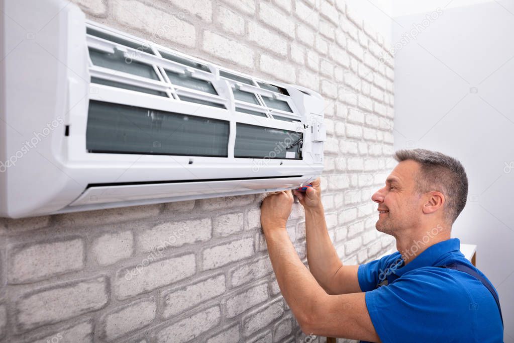 Mature Male Technician Fixing Air Conditioner With Screwdriver