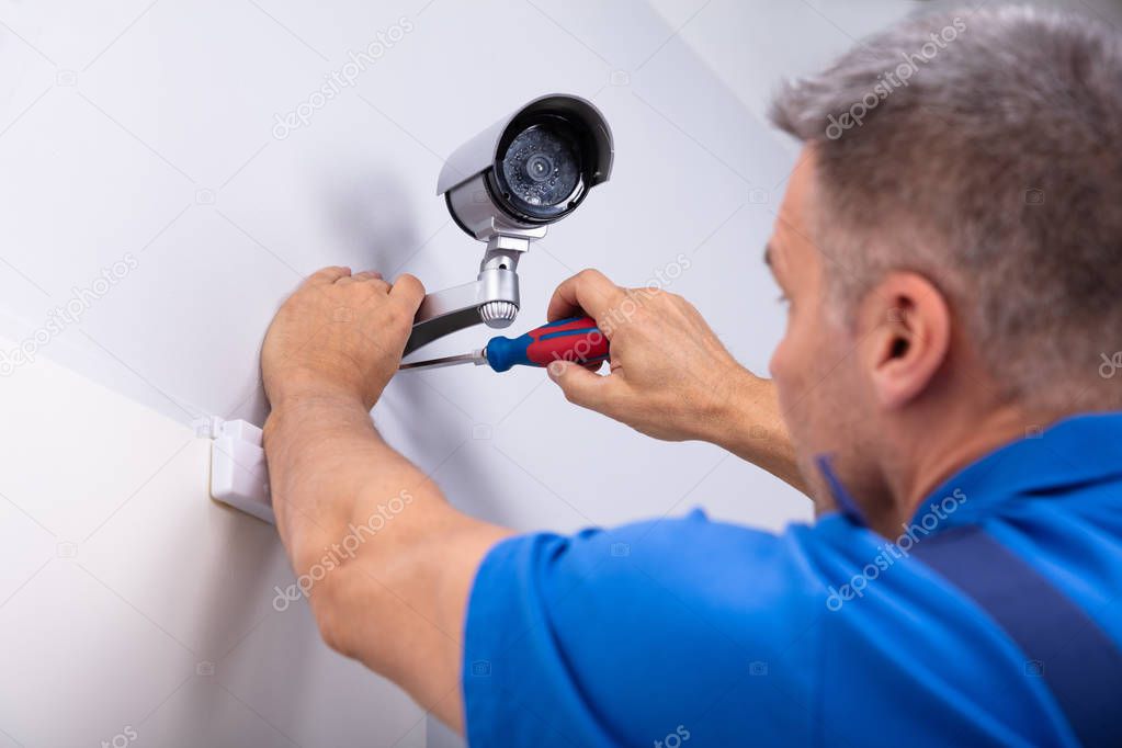 Close-up Of Male Technician Adjusting Cctv Camera On Wall With Screwdriver