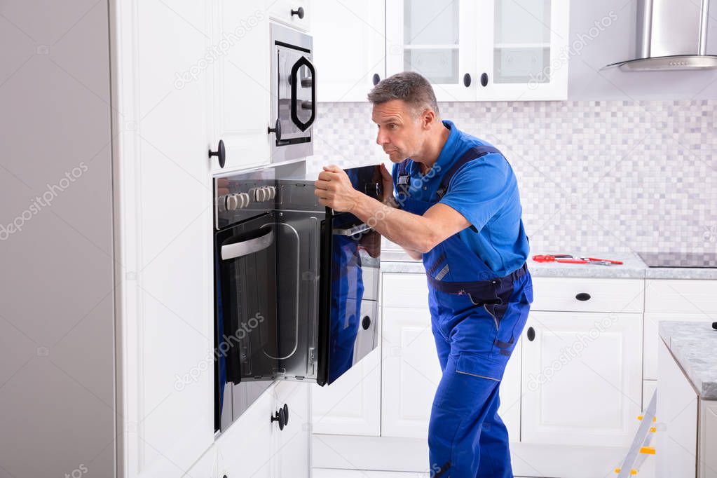 Male Technician Wearing Overall Installing Oven In Kitchen