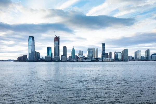 View Of Sky Scrapers In Jersey City With Hudson River Against Cloudy Sky