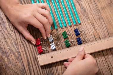 Person Arranging The Colorful Bulldog Clips With Scale On Wooden Desk clipart