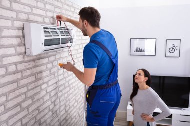Gülümseyen kadın erkek teknisyen ile dijital multimetre evde Klima tamiri bakarak