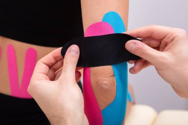 Close-up Of Physiotherapist Applying Kinesiology Tape On Patient's Elbow