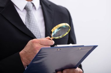 Close-up Of  Businessman Analyzing Document  Through Magnifying Glass At Workplace clipart