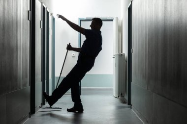 Koridorda yerleri paspaslarken Düşen Olgun Bir Adamın Silueti