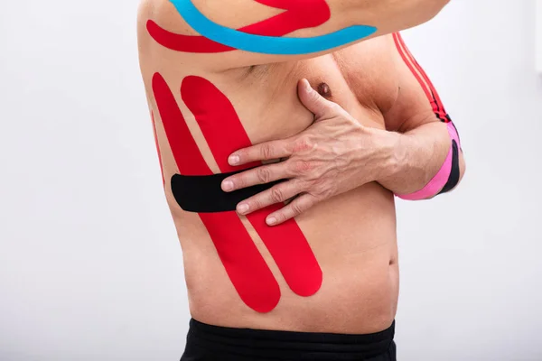 Man Applying Red And Black Kinesiology Therapy Tap On His Ribs. Body shape was altered during retouching