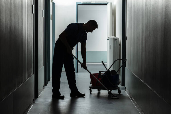 Silhouette Of A Male Janitor Cleaning Corridor